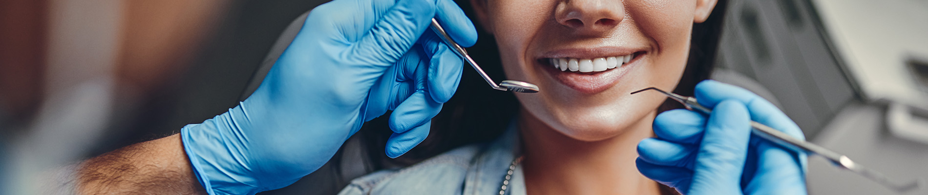 A person is seated in a dental chair, receiving care from a dental professional who stands behind them.