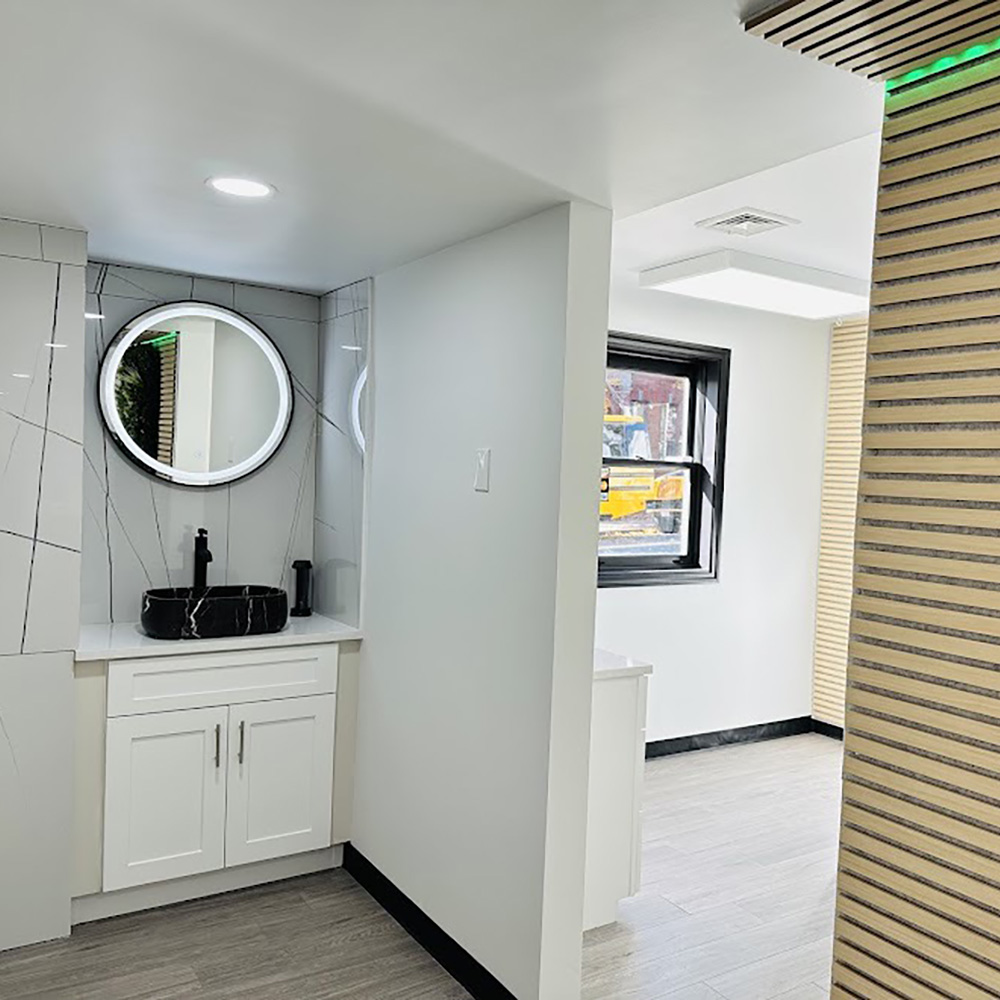 The image shows an interior space with a modern bathroom design featuring a marble countertop, a round mirror, and a black sink.